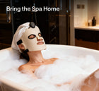 Woman wearing Ulike LED light therapy mask while relaxing in a bubble bath at home