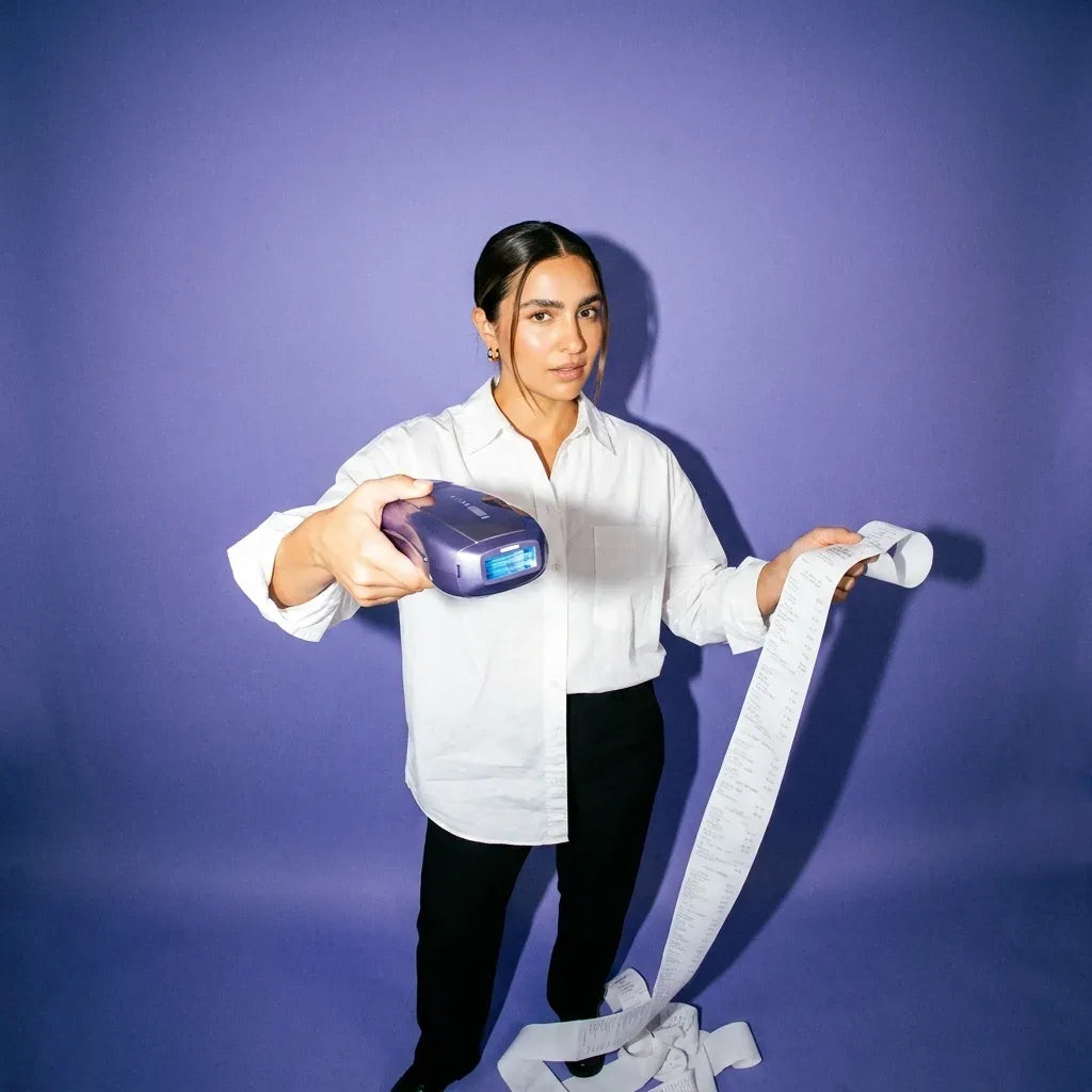 Woman in a white shirt holding the Ulike Air 10 in one hand and a long paper receipt in the other, on a lilac backdrop