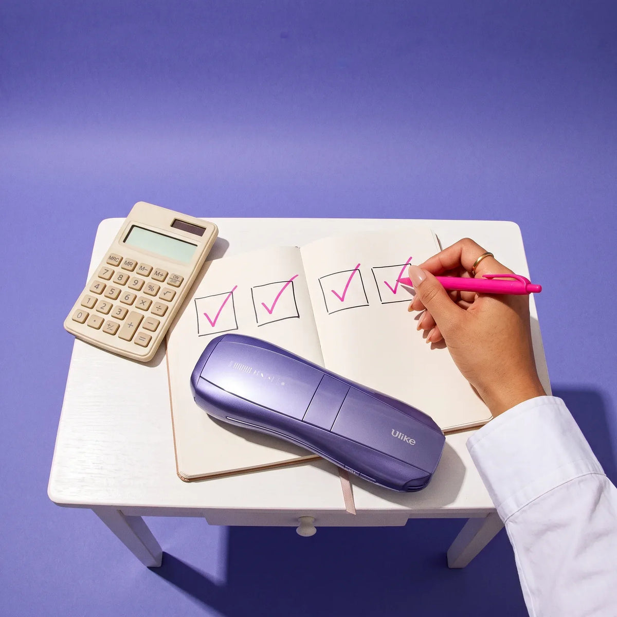 Hand ticking four boxes in pink pen next to a calculator and the Ulike Air 10 on a small white desk