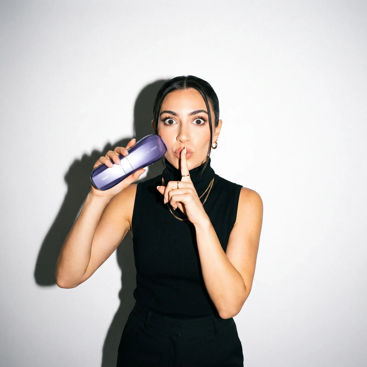 Woman holding the Ulike Air 10 to her cheek with a finger to her lips, wide-eyed