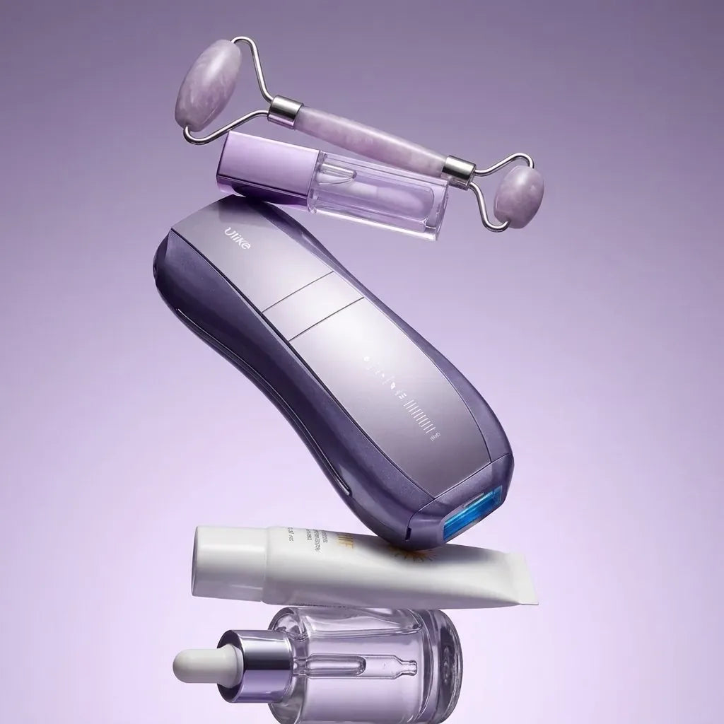 A face roller, lip oil, the Air 10, a sunscreen tube and a serum bottle floating in a stack on lilac