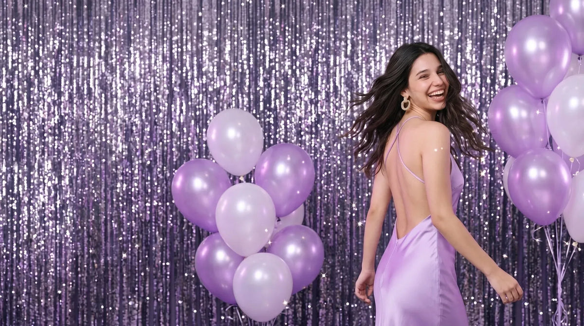 Woman laughing over her shoulder in a lilac slip dress, in front of a glitter curtain and lilac balloons