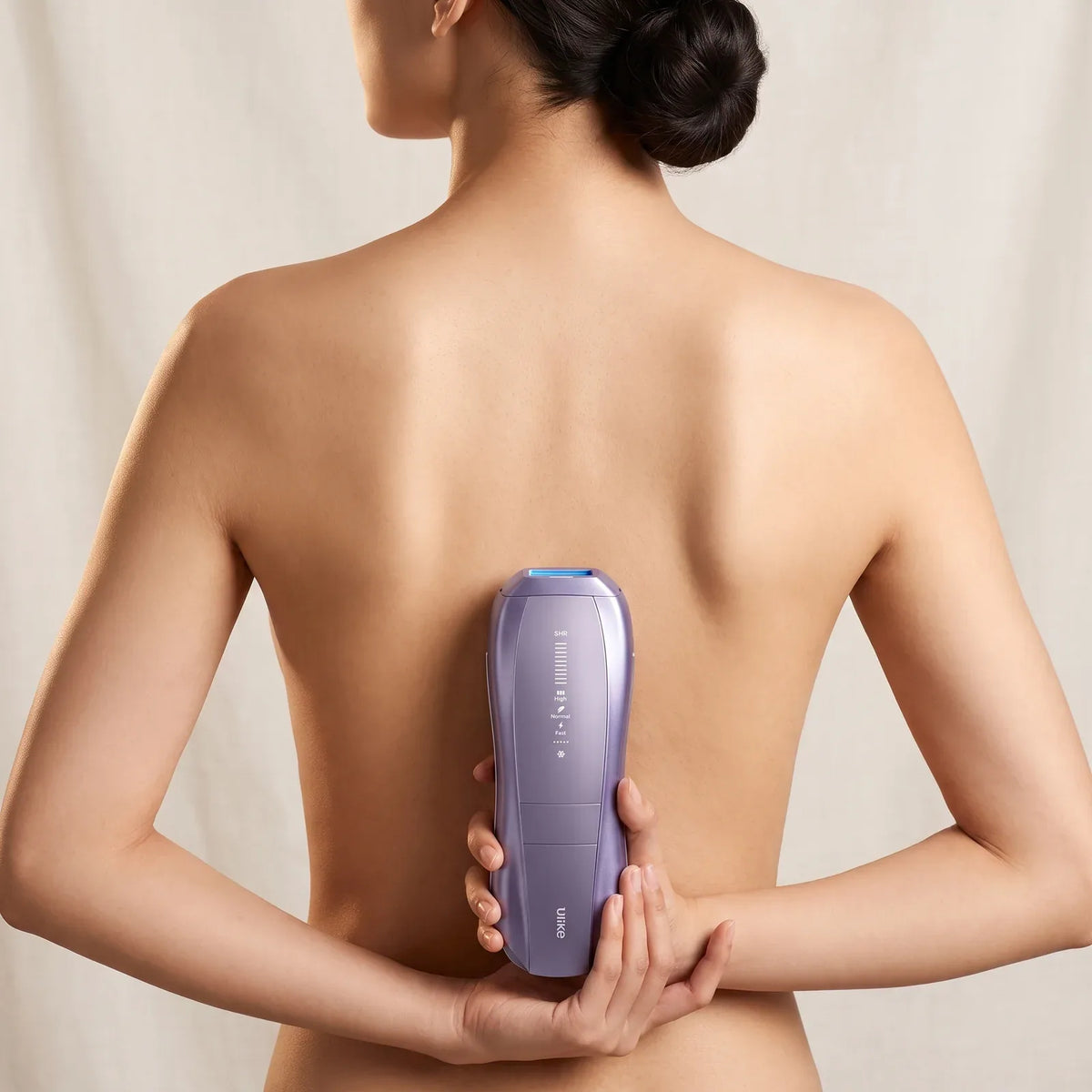 A woman holding the Ulike Air 10 against her back with both hands, cream curtain behind